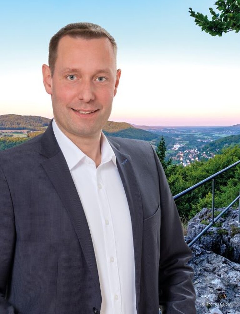 Ein Bild von Landrat Armin Kroder auf der Treppe zum Zankelstein. Er trägt ein weißes Hemd und ein graues Jacket. Im Hintergrund sieht man die Landschaft rund um Pommelsbrunn.