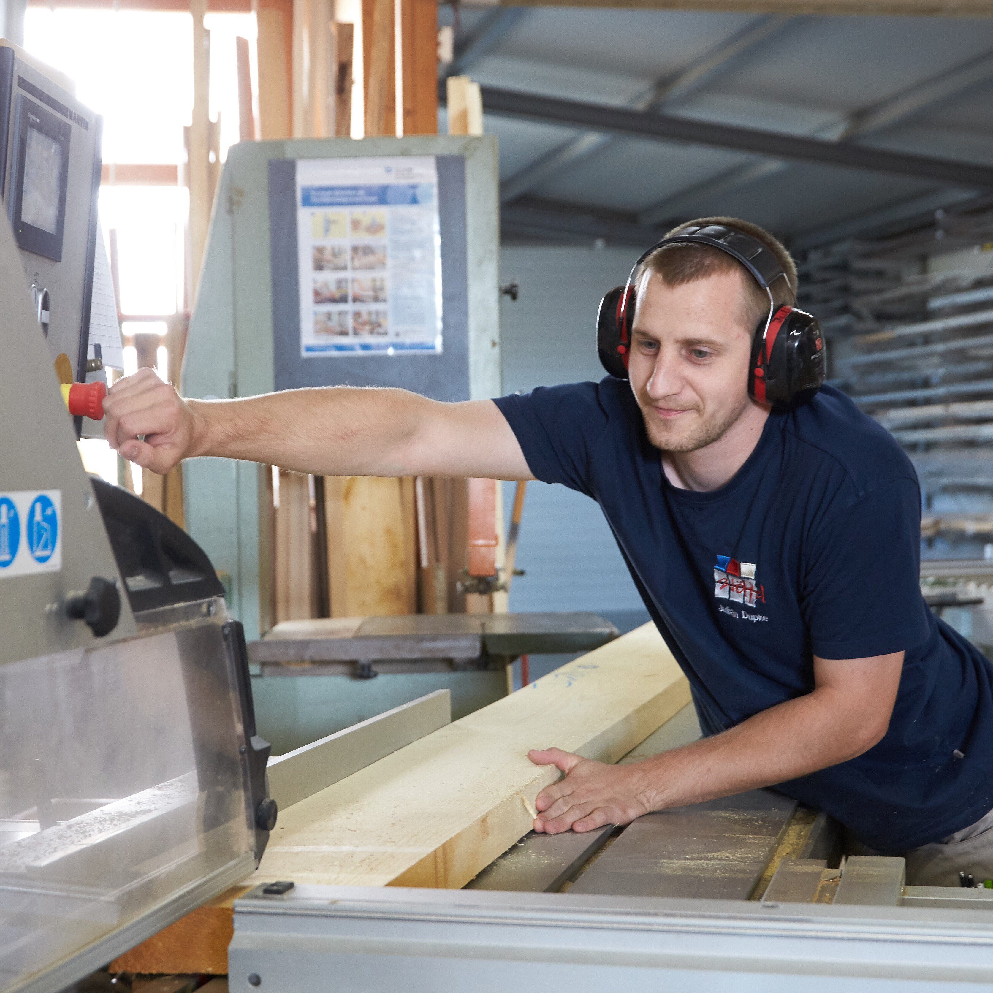 Mann mit Gehörschutz arbeitet an einer Maschine mit Holz.