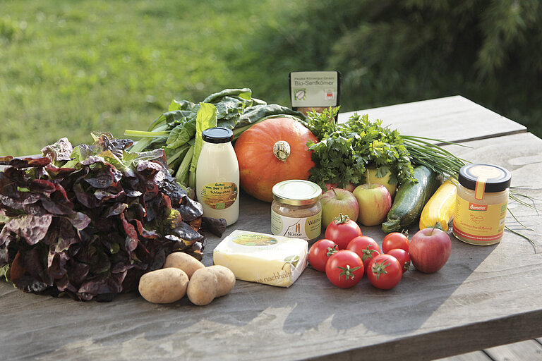 Frisches Gemüse und weitere Lebensmittel stehen auf einem Holztisch. 