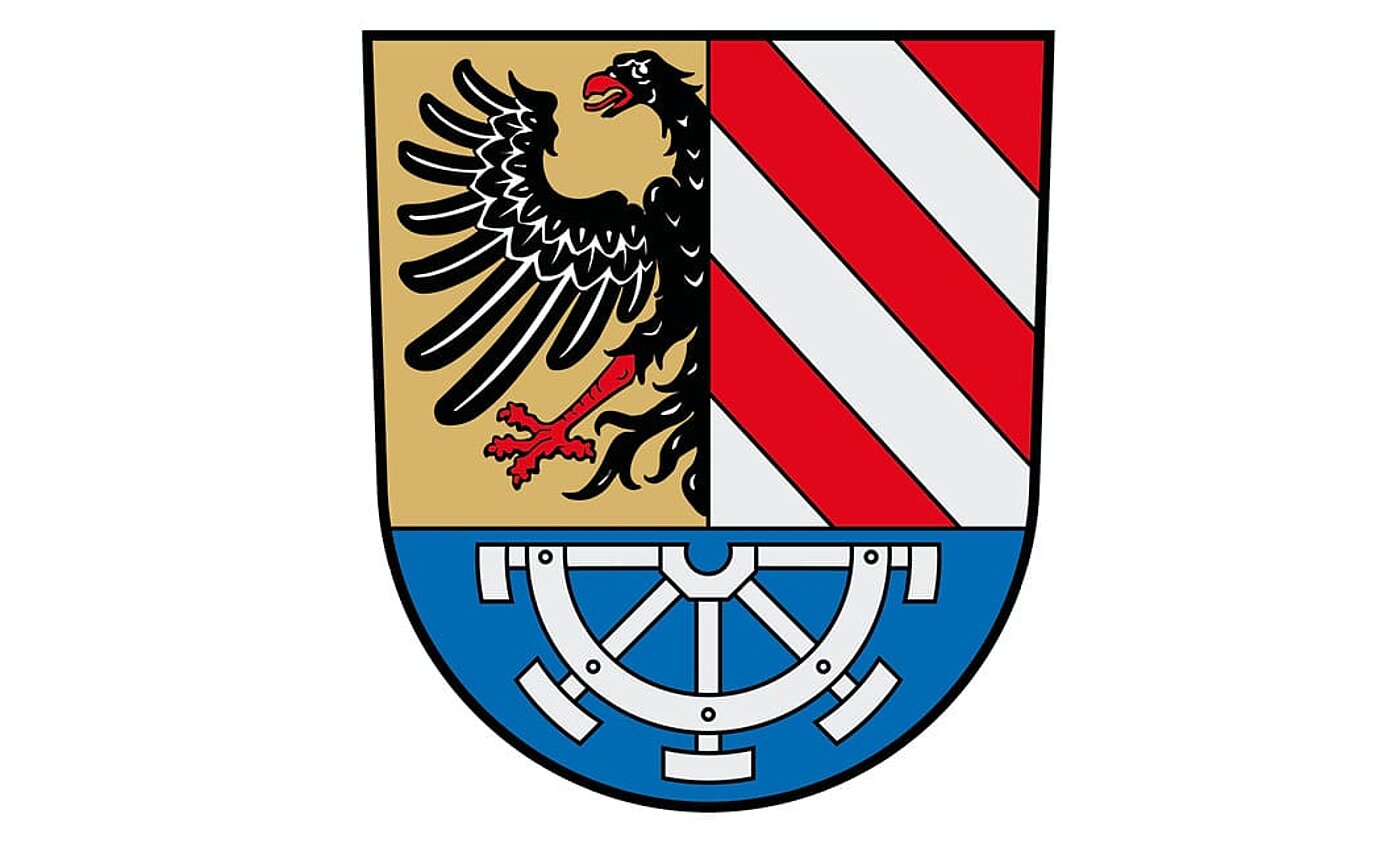 Das Wappen des Landkreises: Über blauem Schildfuß, darin ein unterhalbes silbernes Mühlrad, gespalten; vorne in Gold ein rot bewehrter halber schwarzer Adler am Spalt, hinten fünfmal schräg geteilt von Rot und Silber.