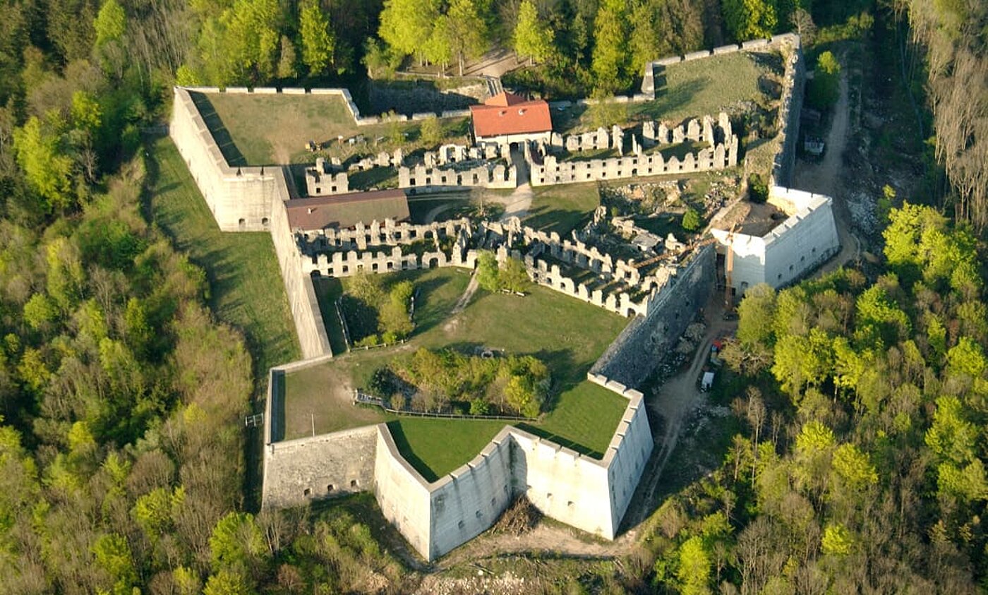 Eine Aufnahme der Festung Rothenberg aus der Vogelperspektive. Rund um die steinernen Festungsmauern ist der Berg mit grünem Wald bewachsen.